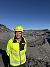 Mann i gul vernejakke og hjelm står foran et steinbrudd under blå himmel.