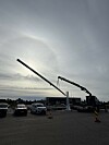 En lang flaggstang løftes av en kran på et industriområde under en overskyet himmel.