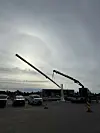 En lang flaggstang løftes av en kran på et industriområde under en overskyet himmel.