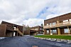 Moderne trebygde boligblokker rundt en asfaltert gårdsplass under en skyet himmel.