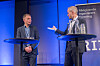 To menn står ved hver sin talerstol på en blåbelyst scene under et RIF-seminar.